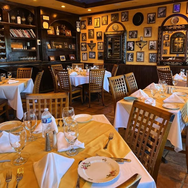 Cafe Vico's dining room with set tables, dark wood, and framed pictures on yellow walls.