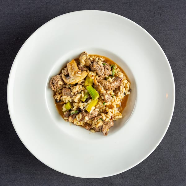 Risotto with beef, mushrooms, and asparagus in a white bowl on a dark background.