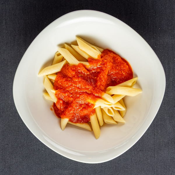 Penne pasta with vibrant red marinara sauce in a white bowl on a dark background.