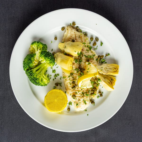Cafe Vico's Italian fish dish with broccoli, artichoke hearts, capers, and lemon on a white plate.