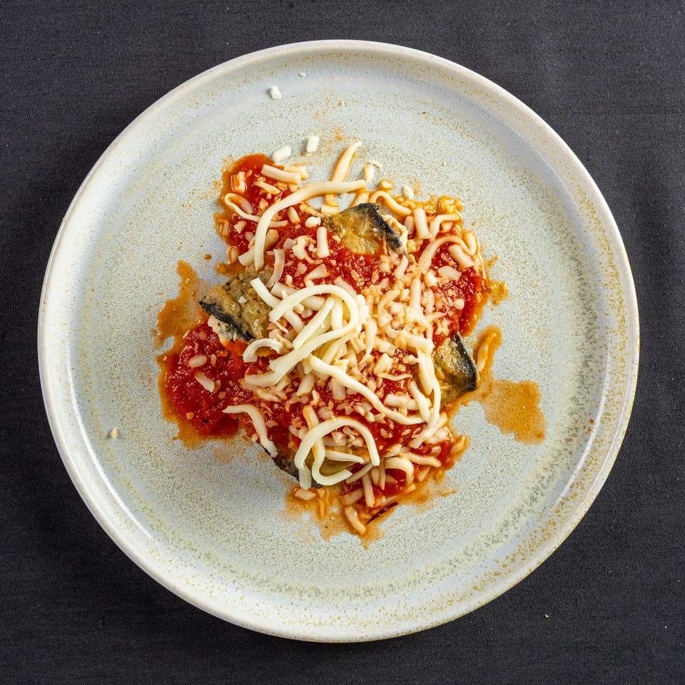 Cafe Vico's Italian eggplant parmesan with rich red sauce and melted cheese on a white plate.