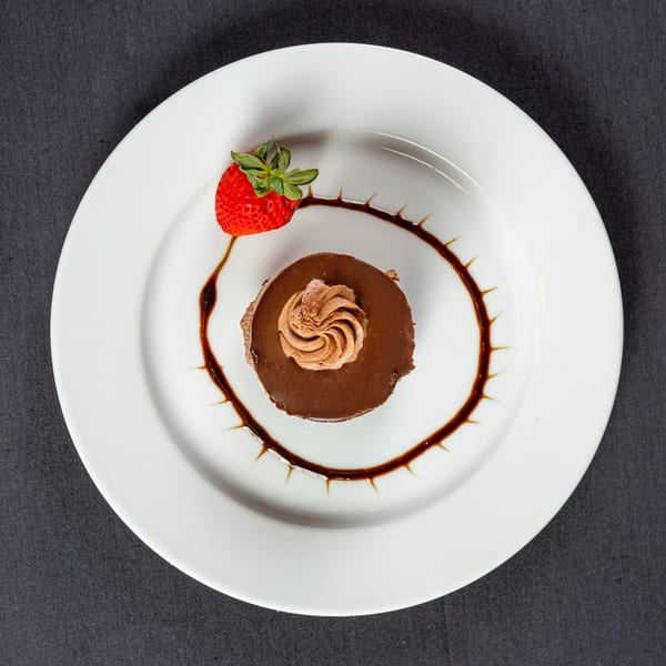 Chocolate dessert with whipped cream, strawberry, and chocolate drizzle on a white plate.