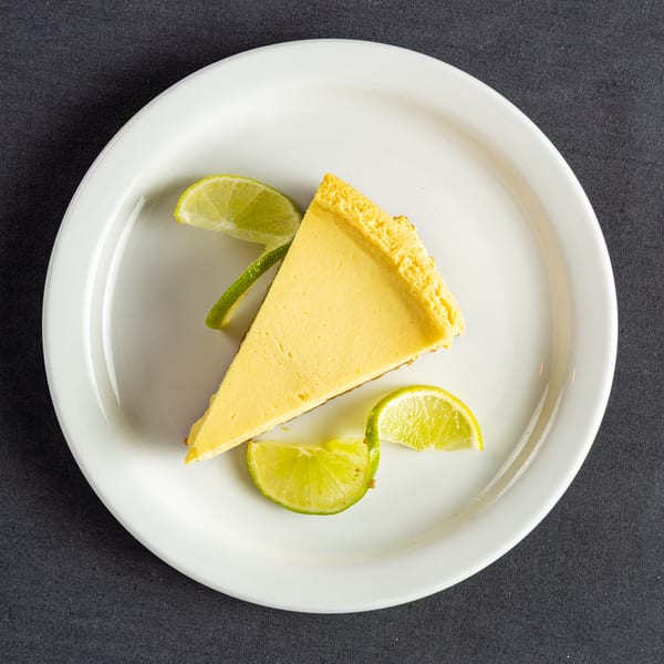 Slice of Key Lime Pie with lime wedges on a white plate, against a dark background.