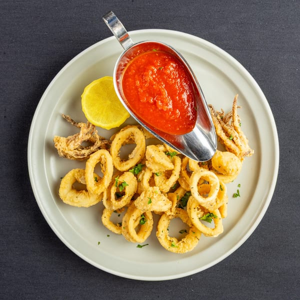Crispy fried calamari rings and tentacles with a side of red marinara sauce and a lemon wedge.