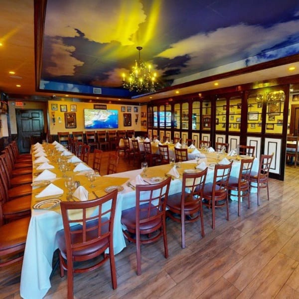 Cafe Vico's private dining room with a long U-shaped table set for guests under a cloud-painted ceiling.