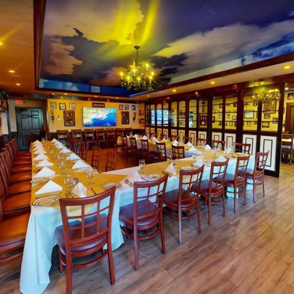 Cafe Vico's private dining room with a long U-shaped table set for guests under a cloud-painted ceiling.