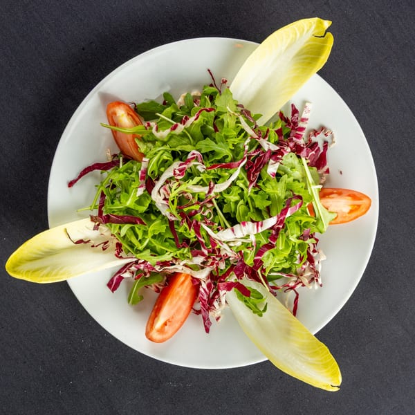 A fresh Italian salad with mixed greens, radicchio, endive, and tomato wedges on a white plate.