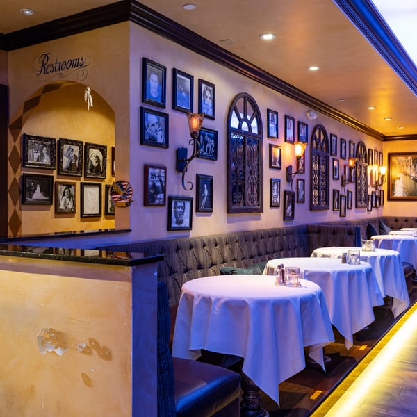 Cozy Italian restaurant interior with framed photos, sconces, and white-clothed tables along a banquette.