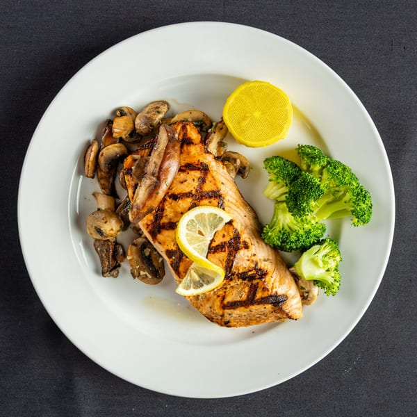 Grilled salmon with lemon slices, sautéed mushrooms, and steamed broccoli on a white plate.